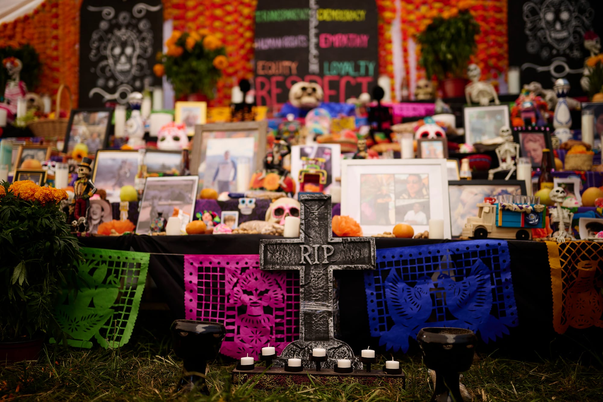 Community ofrenda altar with RIP cross, papel picado, photos of loved ones, and marigolds at Cantina La Martina's final Día de los Muertos