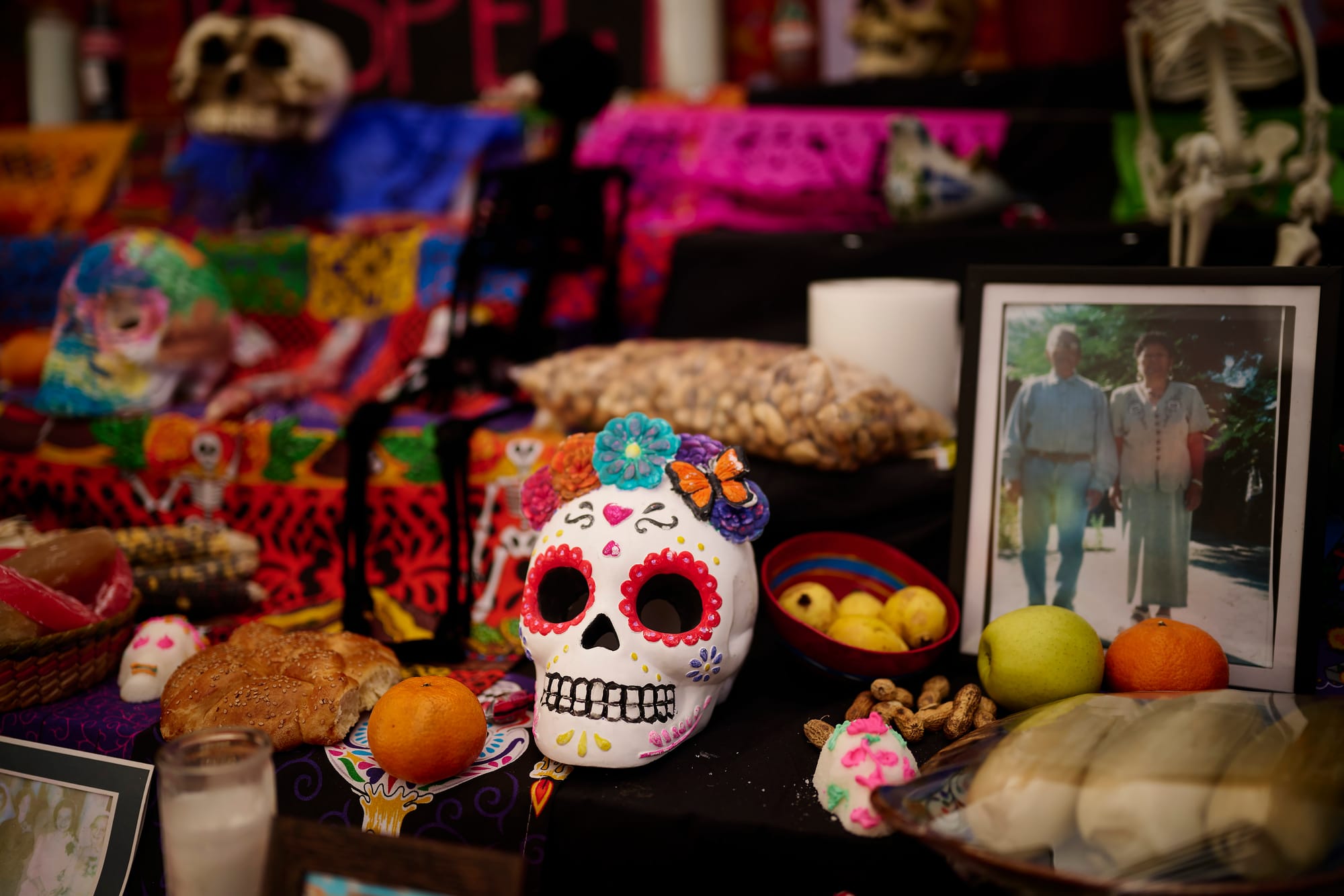 Decorated sugar skull with butterfly and flowers surrounded by pan de muerto and fruit offerings