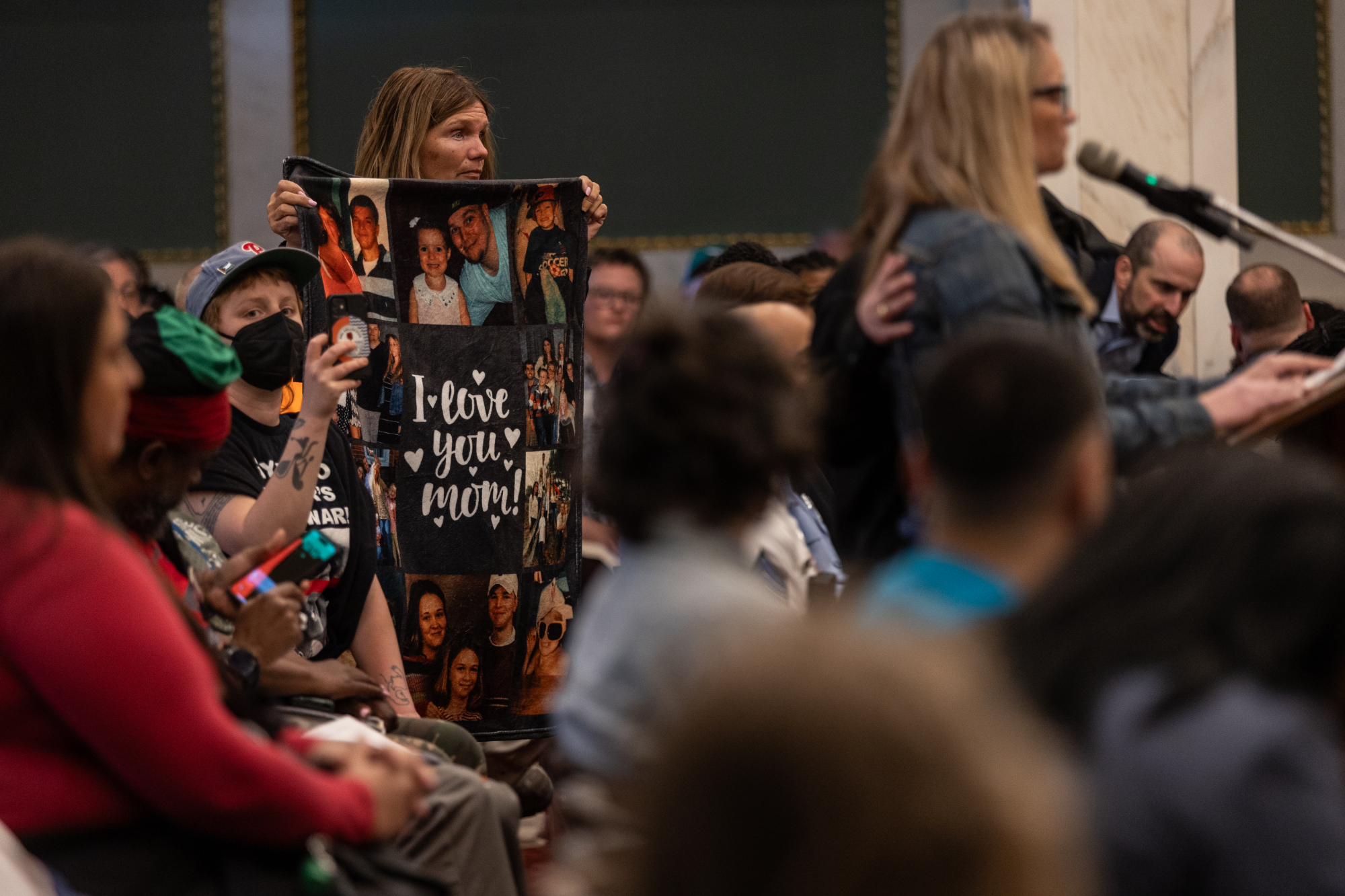 Joey Gabor's mother holds a blanket with family photos during testimony at Quetcy Lozada's town hall on mobile services