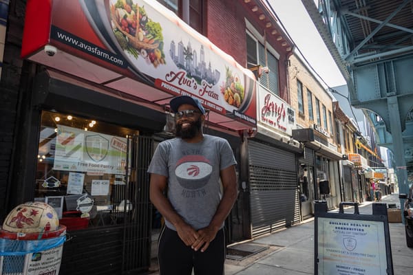 Austin Wright smiles in front of Ava’s Farm, a Kensington Avenue storefront with a red awning and produce-themed signage.