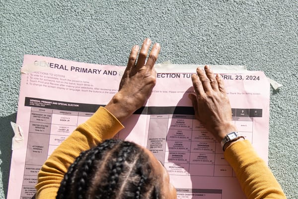 A person in a yellow sweater presses their hands against a printed sample ballot for the Philadelphia primary election.